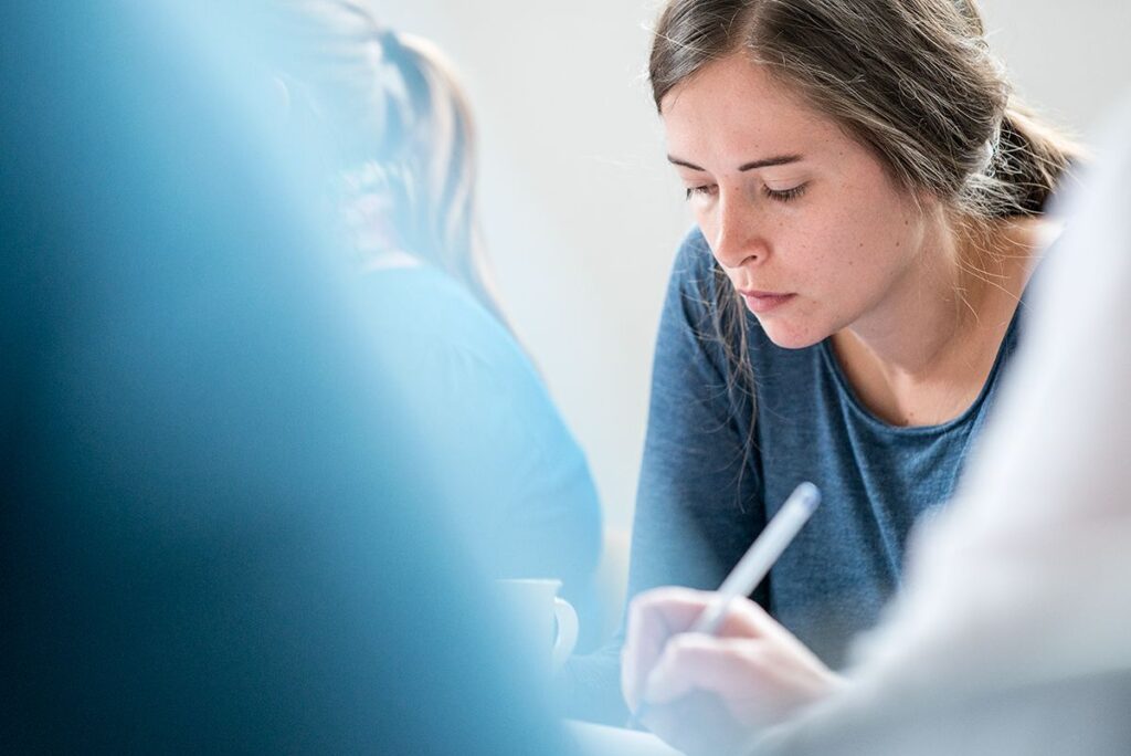 Réunion de plusieurs personnes, une femme est concentrée sur ses notes.