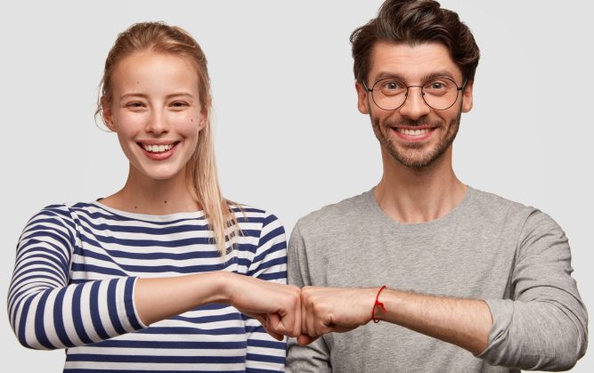Cheerful female and male partners give fist bump, demonstrates their agreement, have broad smiles on faces, rejoice success and cooperation, have good relationship, isolated on white background
